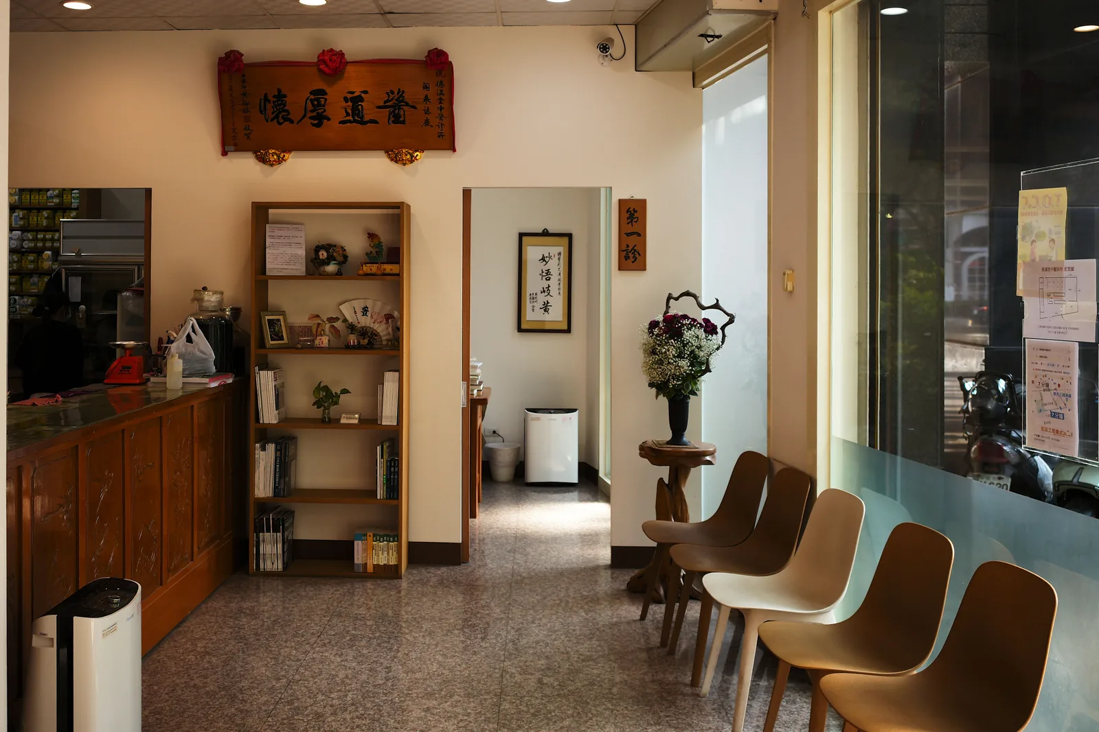 候診大廳全景,左側是掛號櫃檯,右側一排候診椅,底端可見玻璃店面