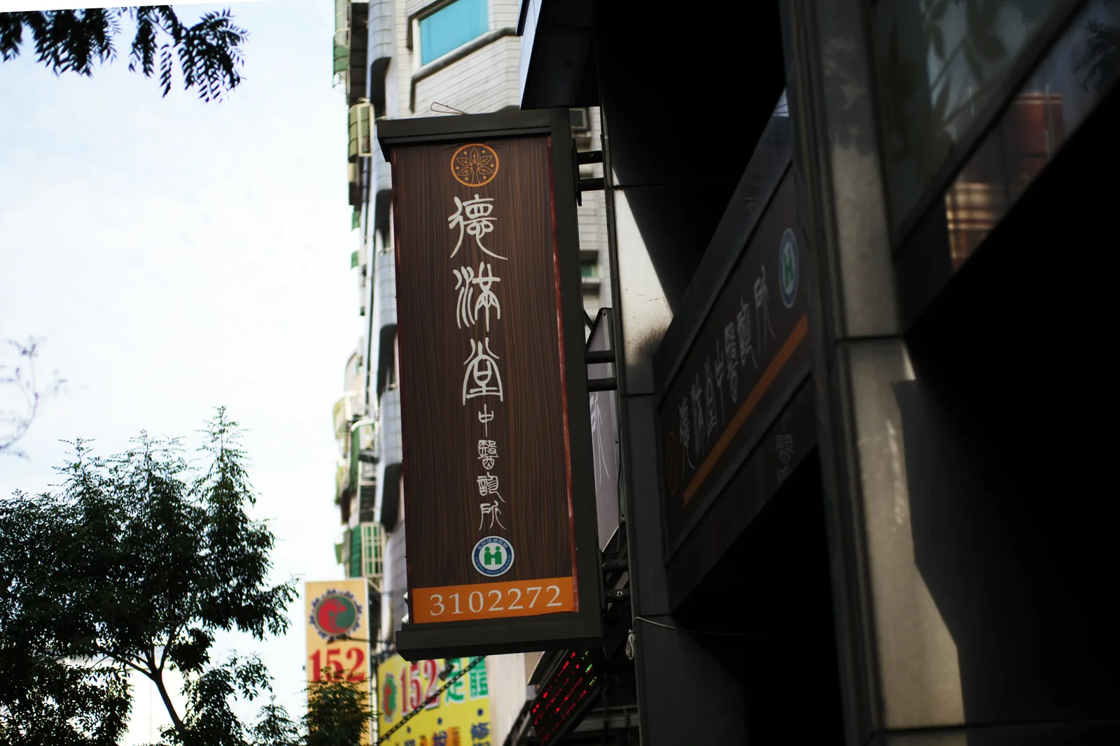 街邊的直式招牌，寫著德滿堂中醫診所與電話